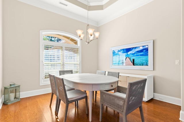 dining area with hardwood / wood-style floors, a tray ceiling, ornamental molding, and a notable chandelier