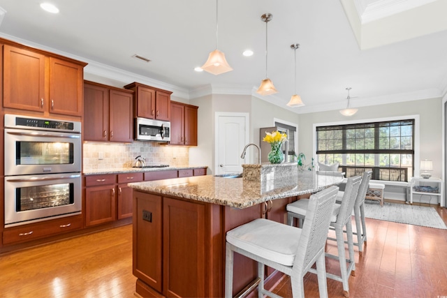 kitchen featuring decorative light fixtures, sink, appliances with stainless steel finishes, and a center island with sink