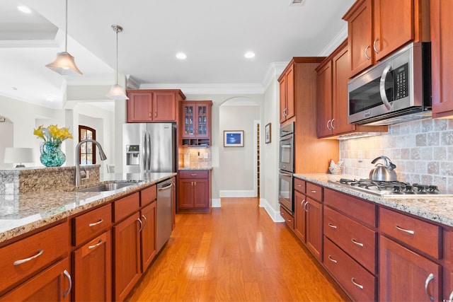 kitchen with sink, hanging light fixtures, light wood-type flooring, appliances with stainless steel finishes, and ornamental molding