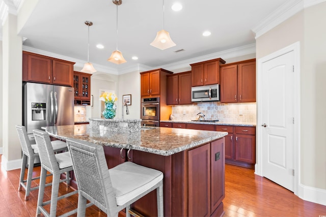 kitchen with hanging light fixtures, appliances with stainless steel finishes, an island with sink, a breakfast bar area, and light stone counters