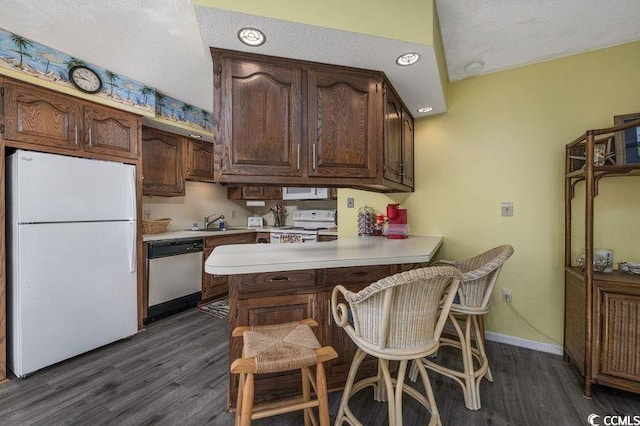 kitchen with a kitchen breakfast bar, dark hardwood / wood-style flooring, kitchen peninsula, and white appliances