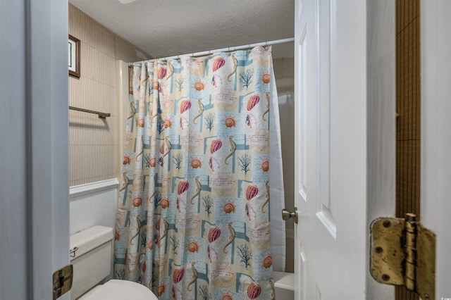 bathroom with a textured ceiling, toilet, and curtained shower