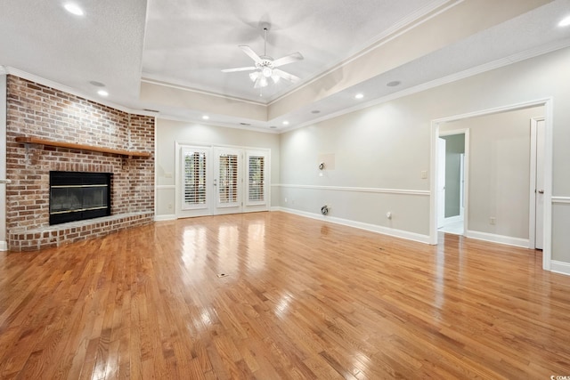 unfurnished living room with a raised ceiling, light hardwood / wood-style floors, crown molding, ceiling fan, and a fireplace