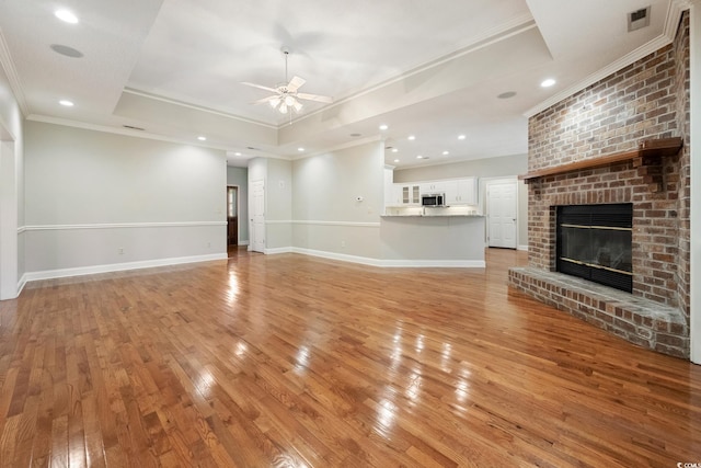 unfurnished living room with light hardwood / wood-style floors, crown molding, ceiling fan, a fireplace, and a tray ceiling