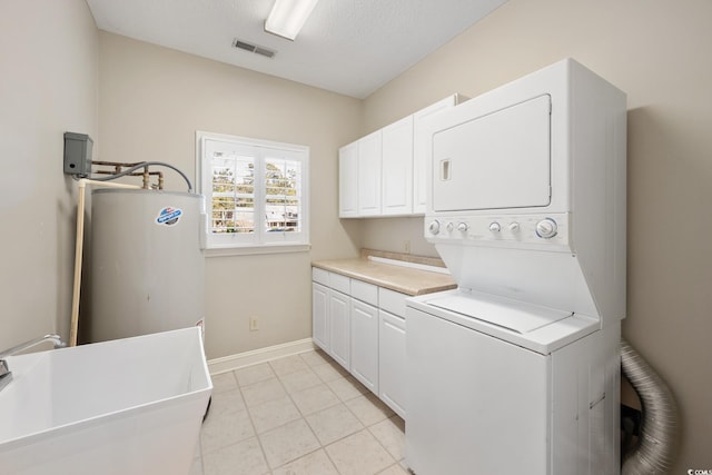 laundry room with cabinets, stacked washer / drying machine, light tile patterned floors, water heater, and a textured ceiling