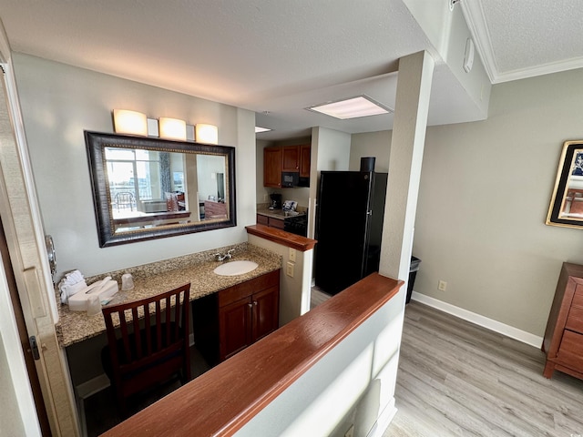 kitchen featuring sink, black refrigerator, ornamental molding, a textured ceiling, and light wood-type flooring