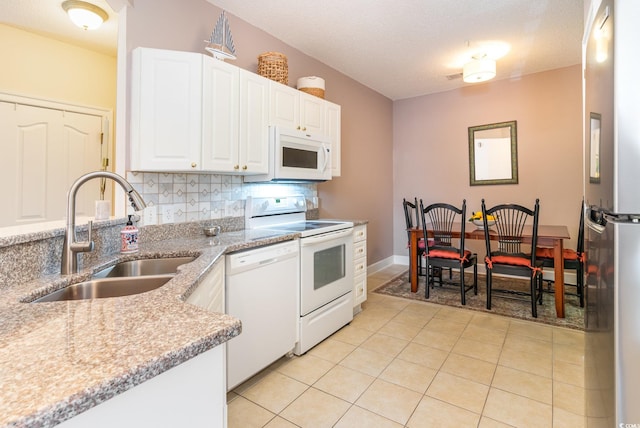 kitchen with white appliances, light stone counters, sink, white cabinetry, and light tile patterned flooring