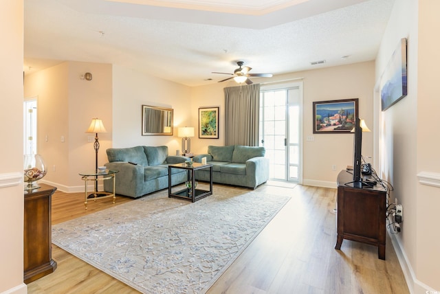 living room featuring ceiling fan, light wood-type flooring, and a textured ceiling