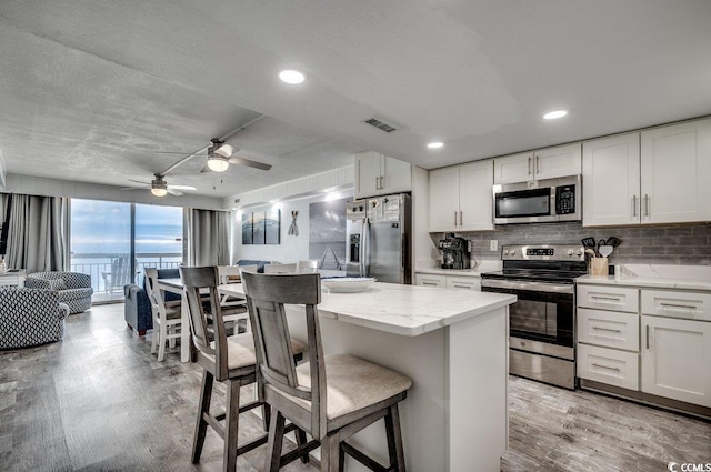 kitchen featuring light wood-style floors, a center island, a breakfast bar area, backsplash, and appliances with stainless steel finishes