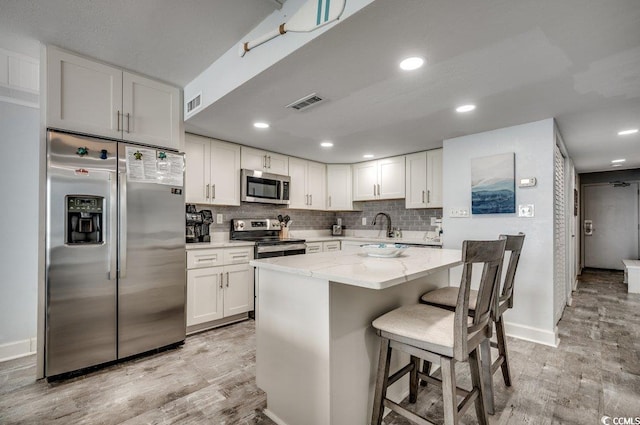 kitchen with visible vents, light wood-type flooring, appliances with stainless steel finishes, and a kitchen bar