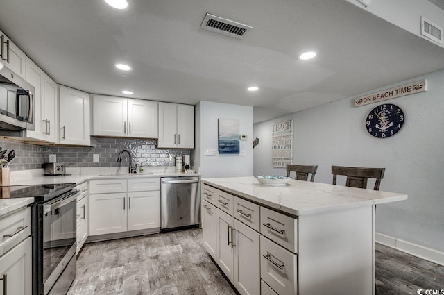 kitchen featuring tasteful backsplash, a sink, visible vents, stainless steel appliances, and light wood-style floors
