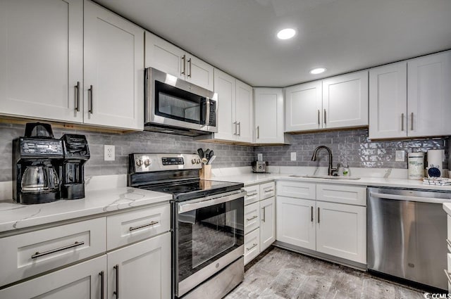 kitchen with tasteful backsplash, light wood-style flooring, stainless steel appliances, a sink, and white cabinetry
