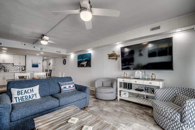 living room with a ceiling fan, visible vents, light wood-style flooring, and baseboards