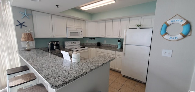 kitchen featuring light tile patterned flooring, a kitchen bar, white cabinetry, kitchen peninsula, and white appliances