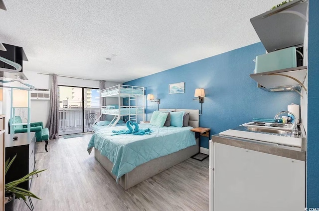 bedroom with sink, a textured ceiling, light wood-type flooring, and access to outside