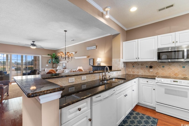 kitchen with white appliances, kitchen peninsula, backsplash, white cabinetry, and sink