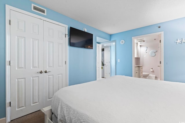 carpeted bedroom featuring a textured ceiling, a closet, and ensuite bath