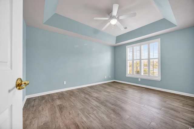 unfurnished room featuring light wood-type flooring, ceiling fan, and a tray ceiling