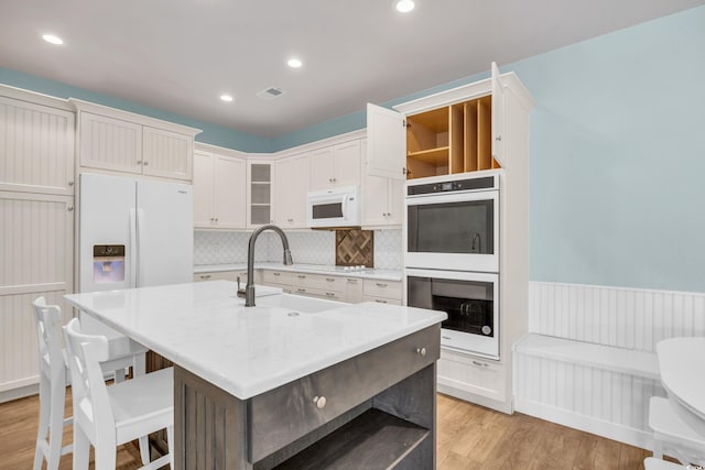 kitchen with sink, white appliances, white cabinetry, light wood-type flooring, and a kitchen island with sink