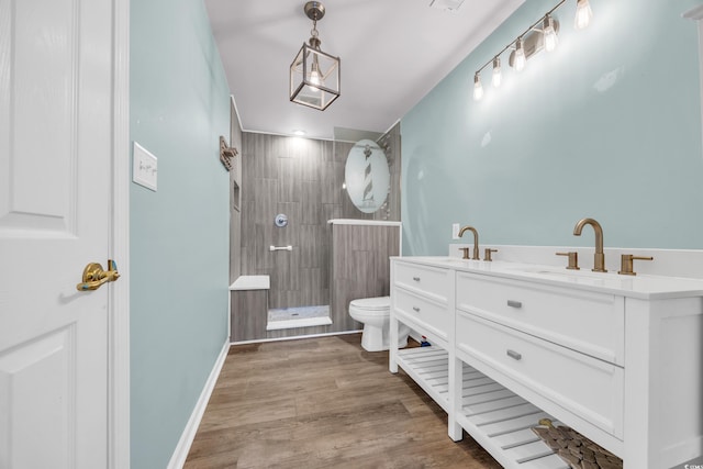 bathroom with toilet, a tile shower, wood-type flooring, and vanity