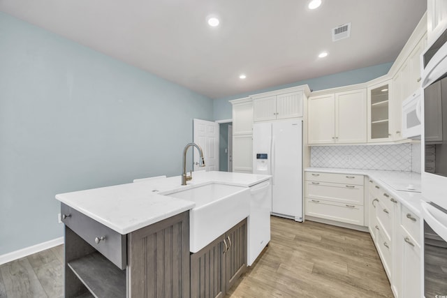 kitchen with white appliances, white cabinets, an island with sink, sink, and light hardwood / wood-style flooring