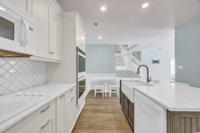 kitchen featuring hardwood / wood-style floors, an island with sink, white appliances, white cabinets, and sink