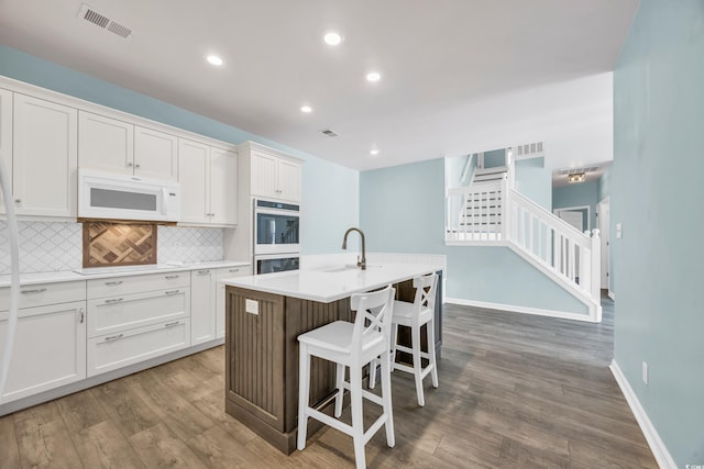 kitchen with a center island with sink, decorative backsplash, white cabinets, and white appliances