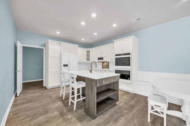 kitchen with tasteful backsplash, white appliances, hardwood / wood-style flooring, a kitchen island with sink, and white cabinets