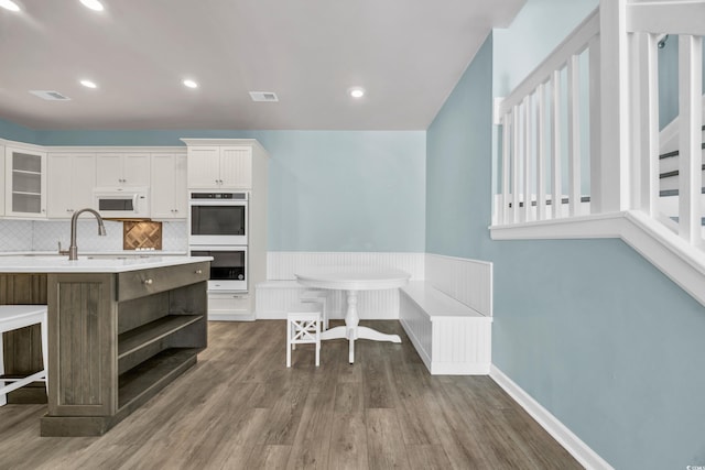 kitchen featuring stainless steel double oven, a breakfast bar, dark hardwood / wood-style flooring, and white cabinetry