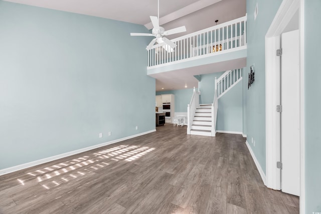 unfurnished living room with ceiling fan, a high ceiling, and light wood-type flooring