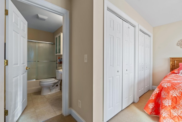 bedroom with connected bathroom, light tile patterned floors, and multiple closets