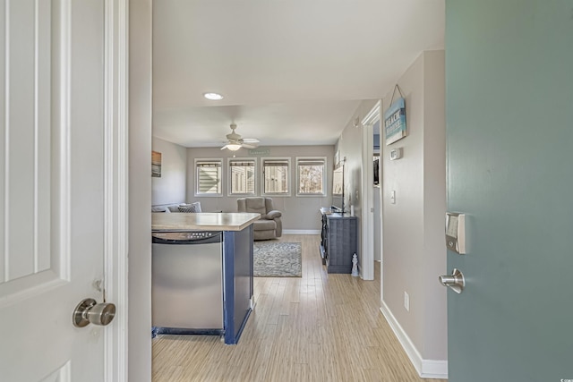 kitchen featuring stainless steel dishwasher, baseboards, light wood-style floors, ceiling fan, and open floor plan