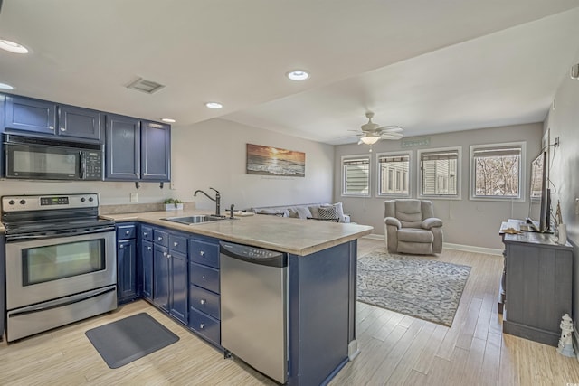 kitchen with appliances with stainless steel finishes, a sink, a peninsula, open floor plan, and light countertops
