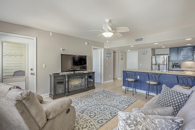 living room featuring ceiling fan, light wood-style flooring, a glass covered fireplace, and baseboards