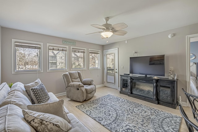 living room featuring ceiling fan, baseboards, a glass covered fireplace, and wood finished floors