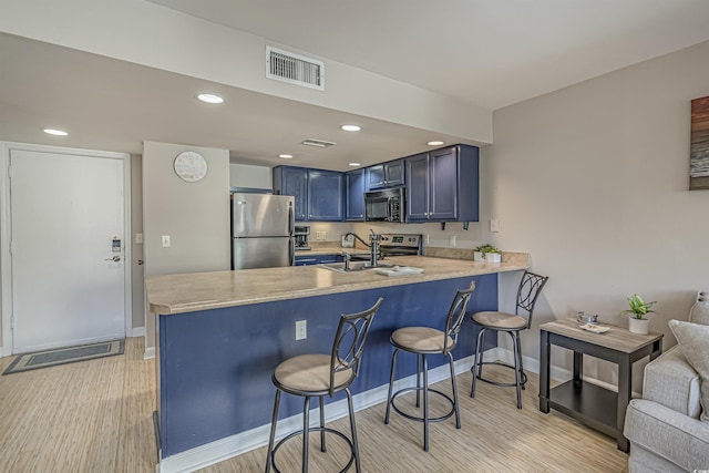 kitchen with stainless steel appliances, light wood-style floors, a peninsula, light countertops, and a breakfast bar area