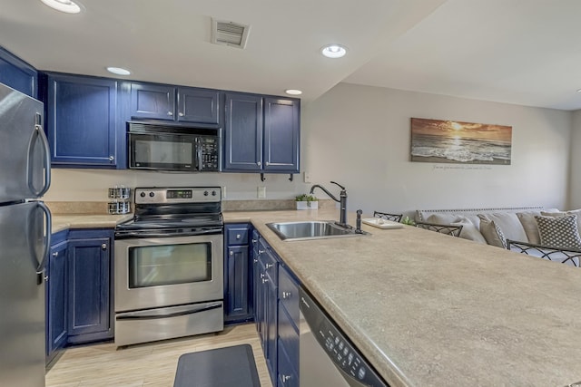 kitchen with stainless steel appliances, a sink, blue cabinets, light wood finished floors, and light countertops