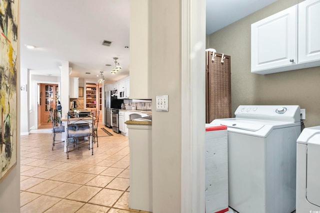 washroom with light tile patterned floors, washer and dryer, and cabinets