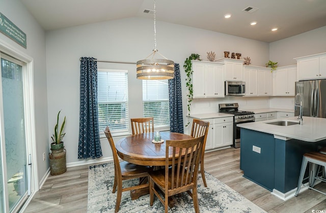 kitchen with appliances with stainless steel finishes, white cabinetry, sink, hanging light fixtures, and a kitchen island with sink