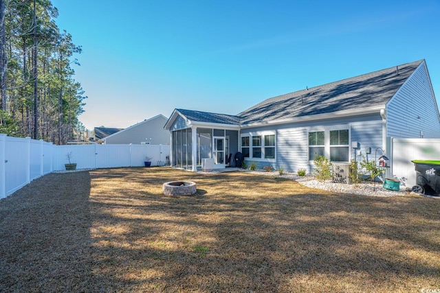 back of property featuring a fire pit, a lawn, and a sunroom