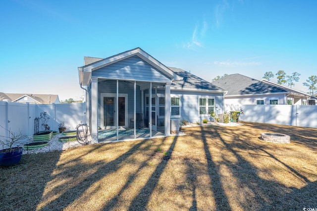 rear view of house featuring a sunroom, a yard, and a fire pit