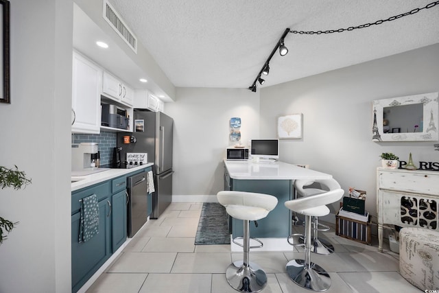 kitchen featuring appliances with stainless steel finishes, tasteful backsplash, white cabinetry, a kitchen breakfast bar, and a textured ceiling