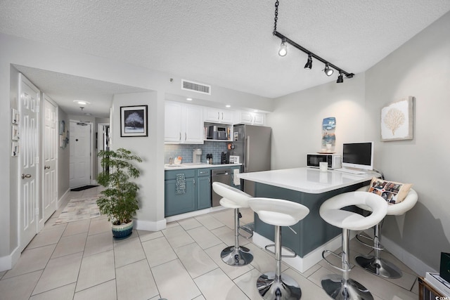 kitchen featuring a breakfast bar, a textured ceiling, white cabinets, stainless steel appliances, and backsplash