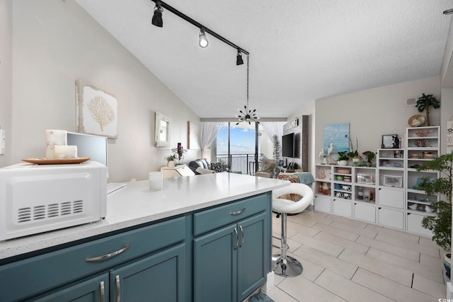 kitchen featuring a kitchen breakfast bar, a notable chandelier, track lighting, a textured ceiling, and blue cabinets