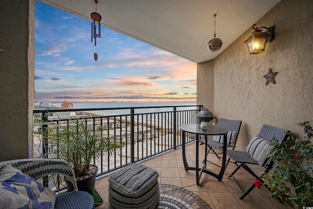 balcony at dusk featuring a water view