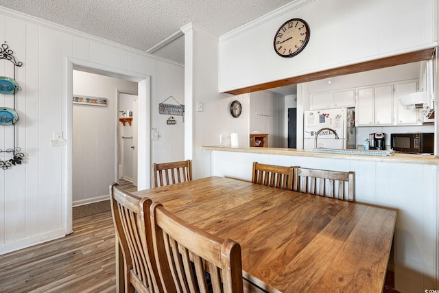 dining space featuring a textured ceiling, dark hardwood / wood-style flooring, crown molding, and wooden walls