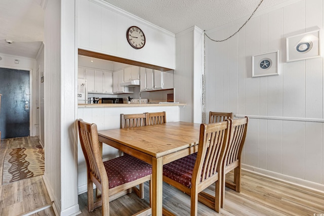 dining area with a textured ceiling, light hardwood / wood-style flooring, and ornamental molding