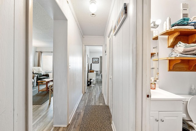 hallway with a textured ceiling, light hardwood / wood-style flooring, and ornamental molding