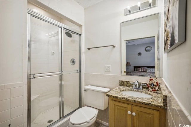 bathroom featuring tile walls, vanity, a shower with shower door, and toilet