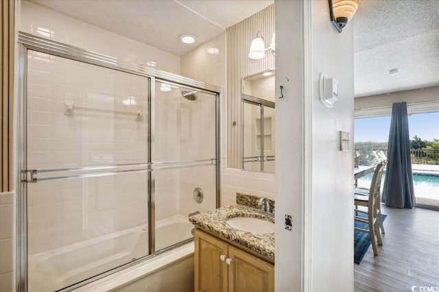 bathroom with hardwood / wood-style floors, a textured ceiling, enclosed tub / shower combo, and vanity